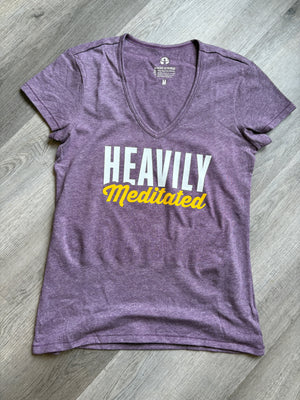 Purple t-shirt with 'HEAVILY Meditated' text on a wooden floor