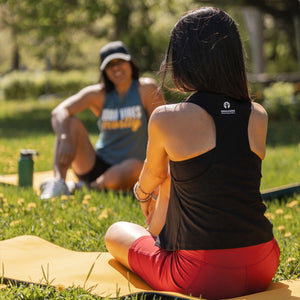 Back view of a black cropped racerback tank. Model is a yoga instructor, chatting with friends in a park after class.