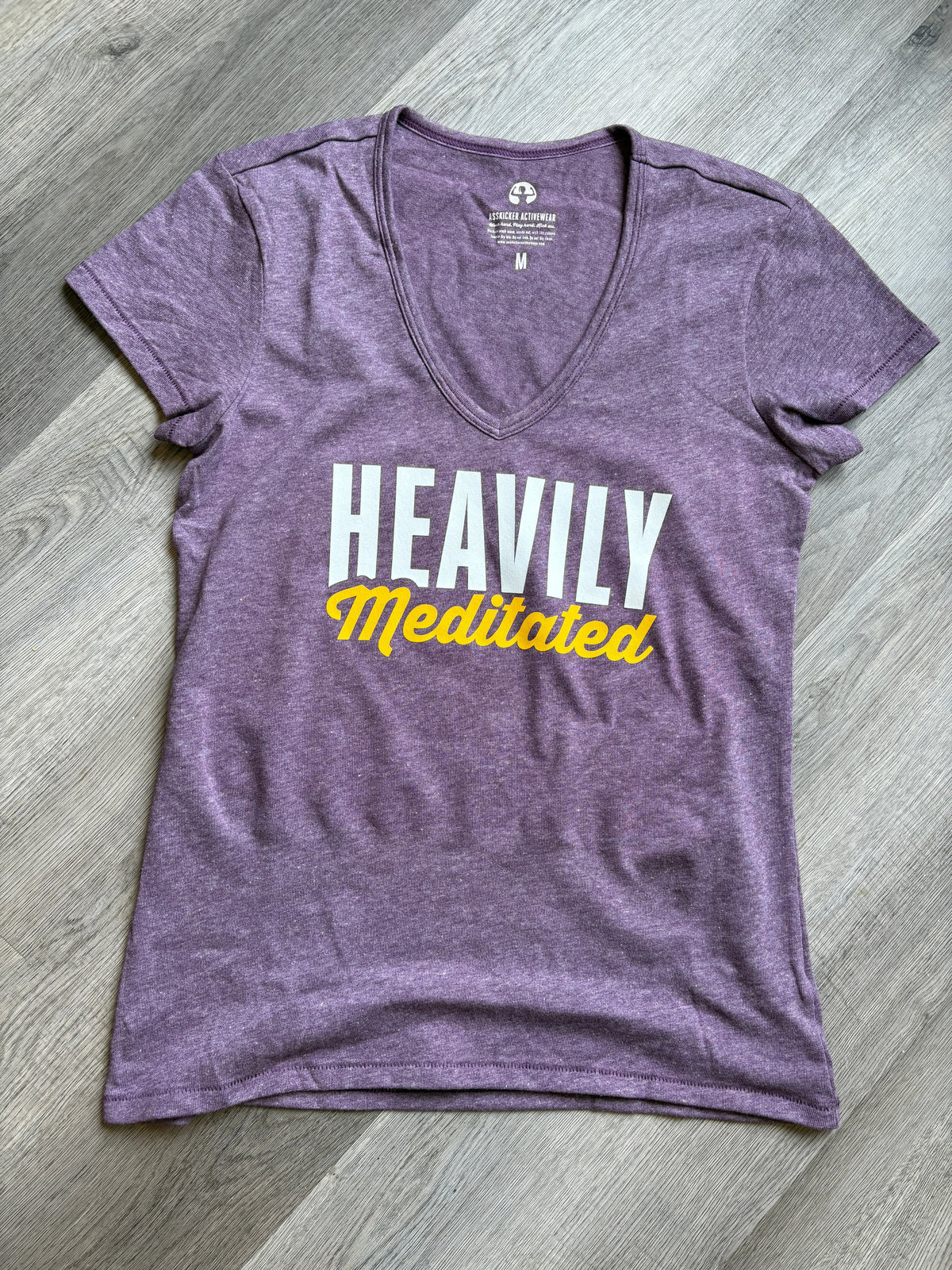Purple t-shirt with 'HEAVILY Meditated' text on a wooden floor