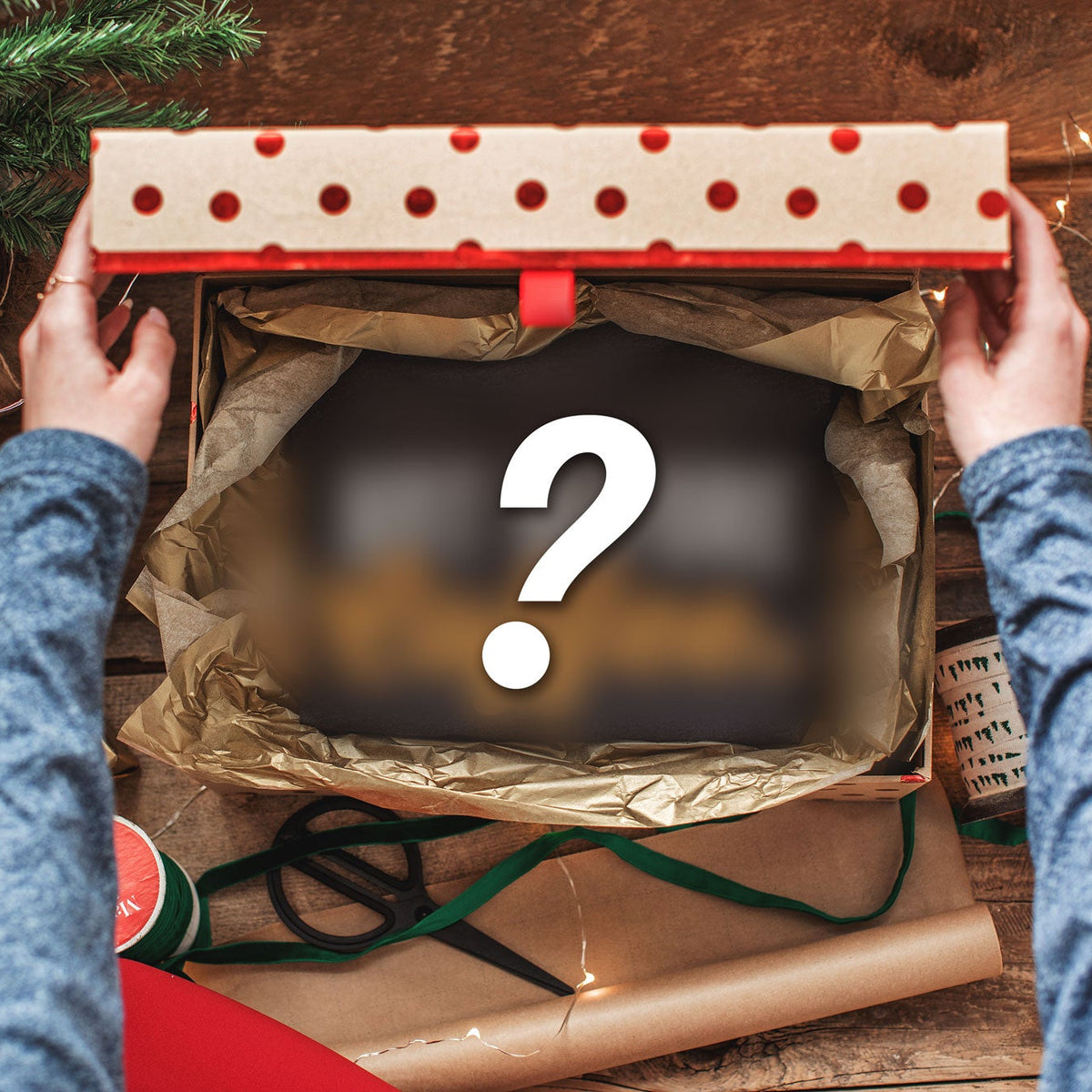 A top-down view of a person's hands holding open a gift box filled with brown tissue paper, surrounded by Christmas decorations, wrapping paper, and a large question mark graphic overlay.