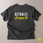 A dark charcoal gray t-shirt laid flat on a light beige background, featuring the text 'ACTUALLY, I can.' in white and yellow with a small yellow flexing bicep graphic.