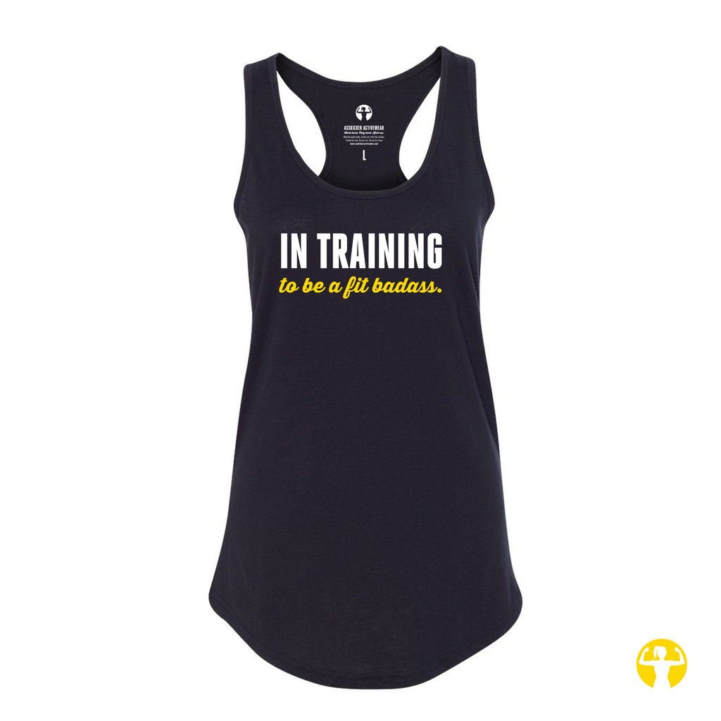 A black racerback tank top with the text In Training to be a Fit Badass' printed on the front in white and yellow, displayed on a solid white background.