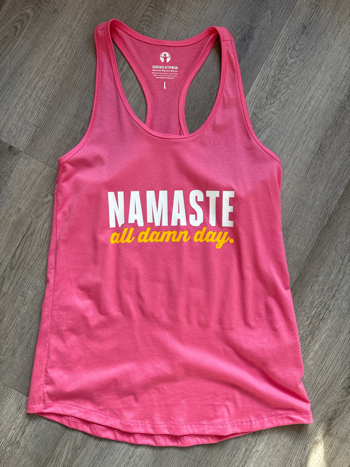 Pink tank top with &#39;NAMASTE all damn day&#39; text on a wooden surface
