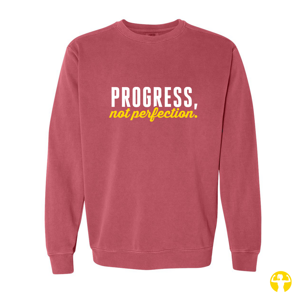 A dusty rose crewneck sweatshirt featuring the text 'PROGRESS, not perfection.' printed on the chest in white and yellow, displayed against a solid white background.
