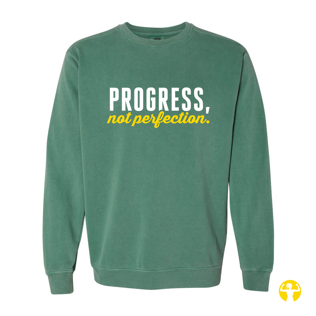A green crewneck sweatshirt with the text 'PROGRESS, not perfection.' printed on the chest in white and yellow, shown against a plain white background.