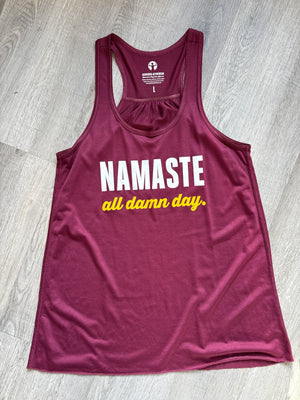 Maroon tank top with 'Namaste all damn day' text on a wooden floor.