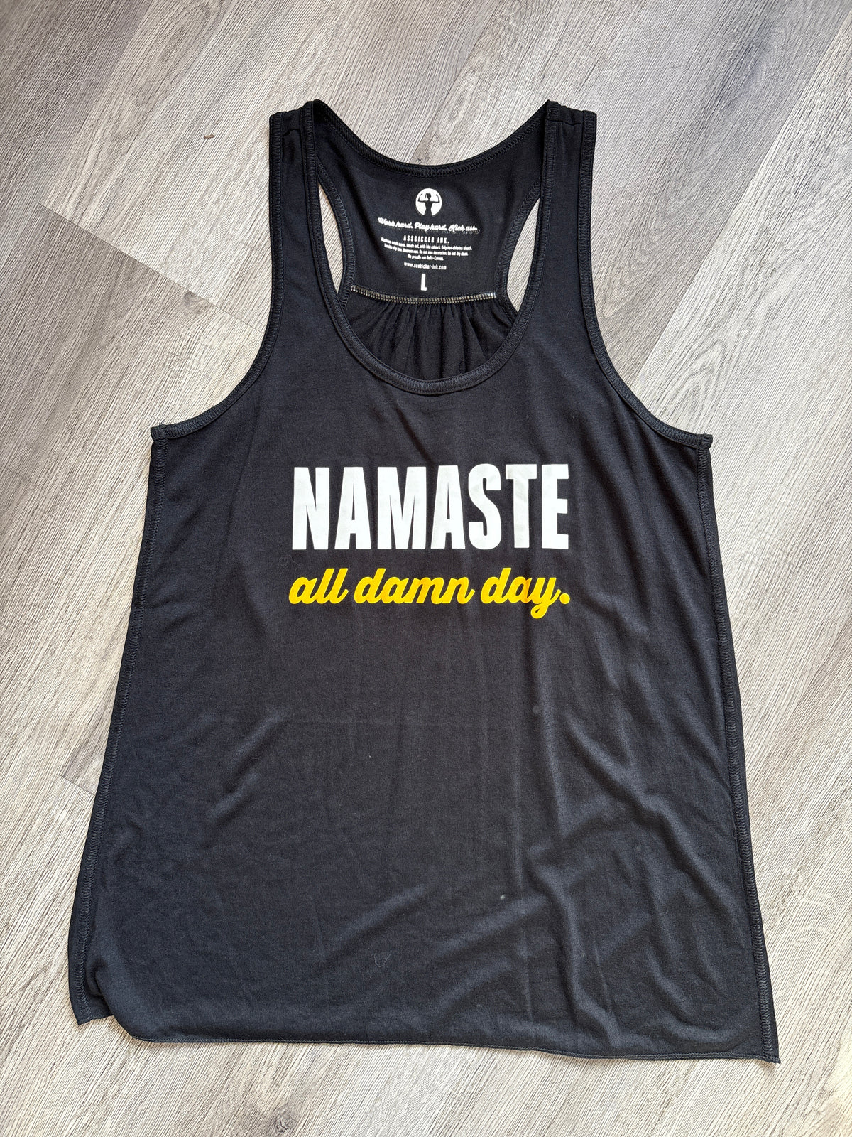 Black tank top with &#39;Namaste all damn day&#39; text on a wooden floor