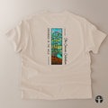 An off-white short-sleeve t-shirt laid flat on a neutral beige background, showing the back side with a colorful graphic of pine trees and the text 'GROUNDED IN THE WILD' and 'The Canvas Collection'.