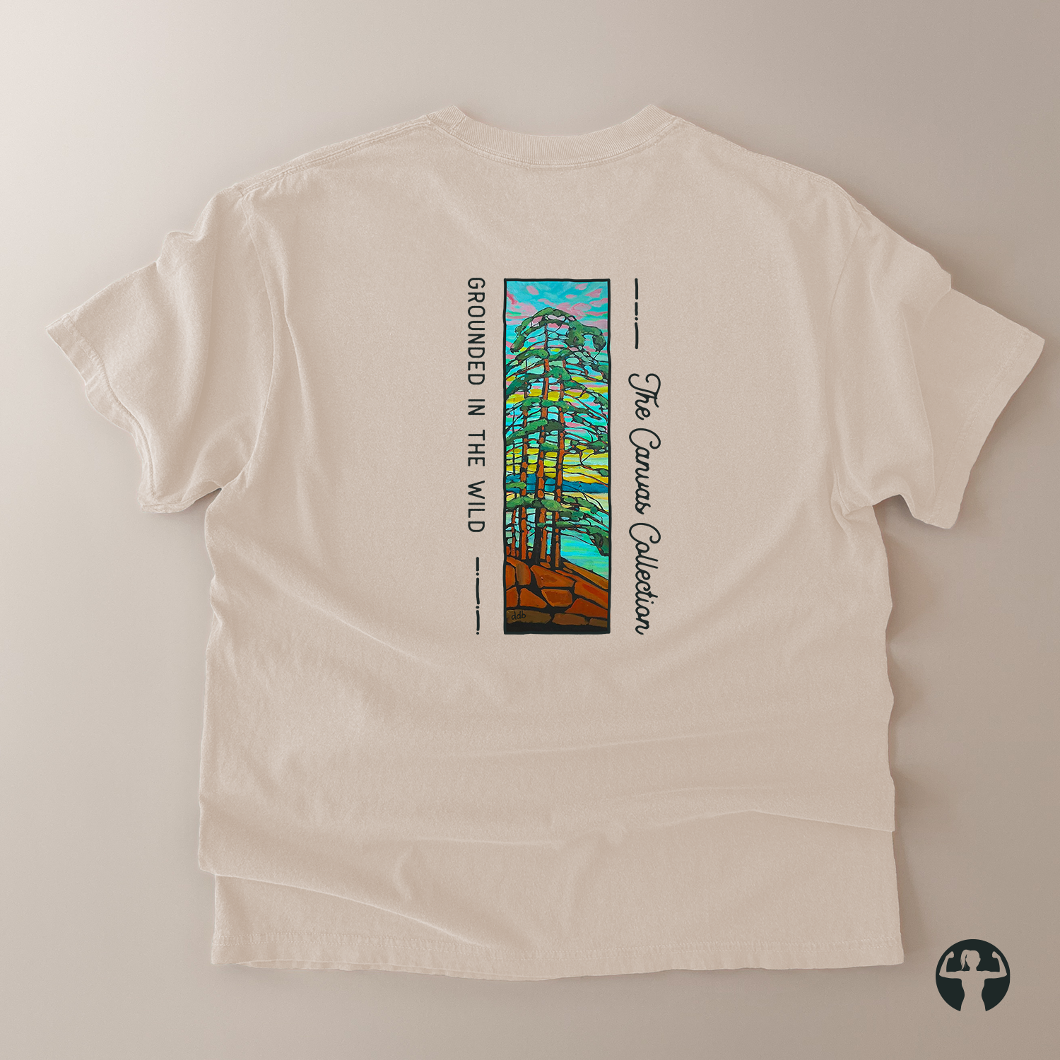 An off-white short-sleeve t-shirt laid flat on a neutral beige background, showing the back side with a colorful graphic of pine trees and the text 'GROUNDED IN THE WILD' and 'The Canvas Collection'.